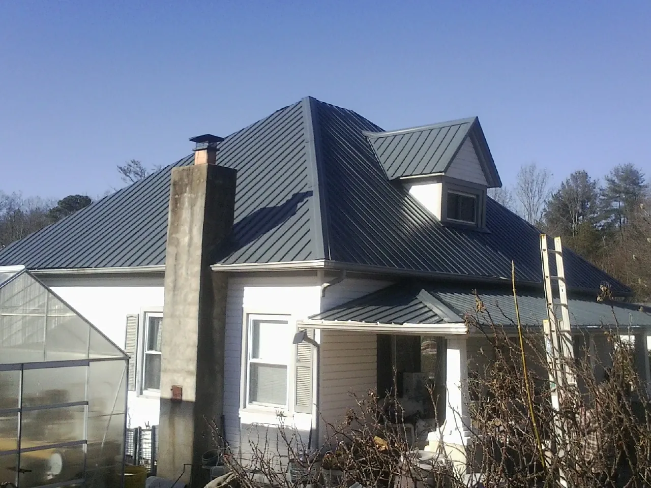 Dark blue standing seam metal roof on a white farmhouse with dormer — Slate & Tile Roof Repair by Roofing Brothers in Louisburg