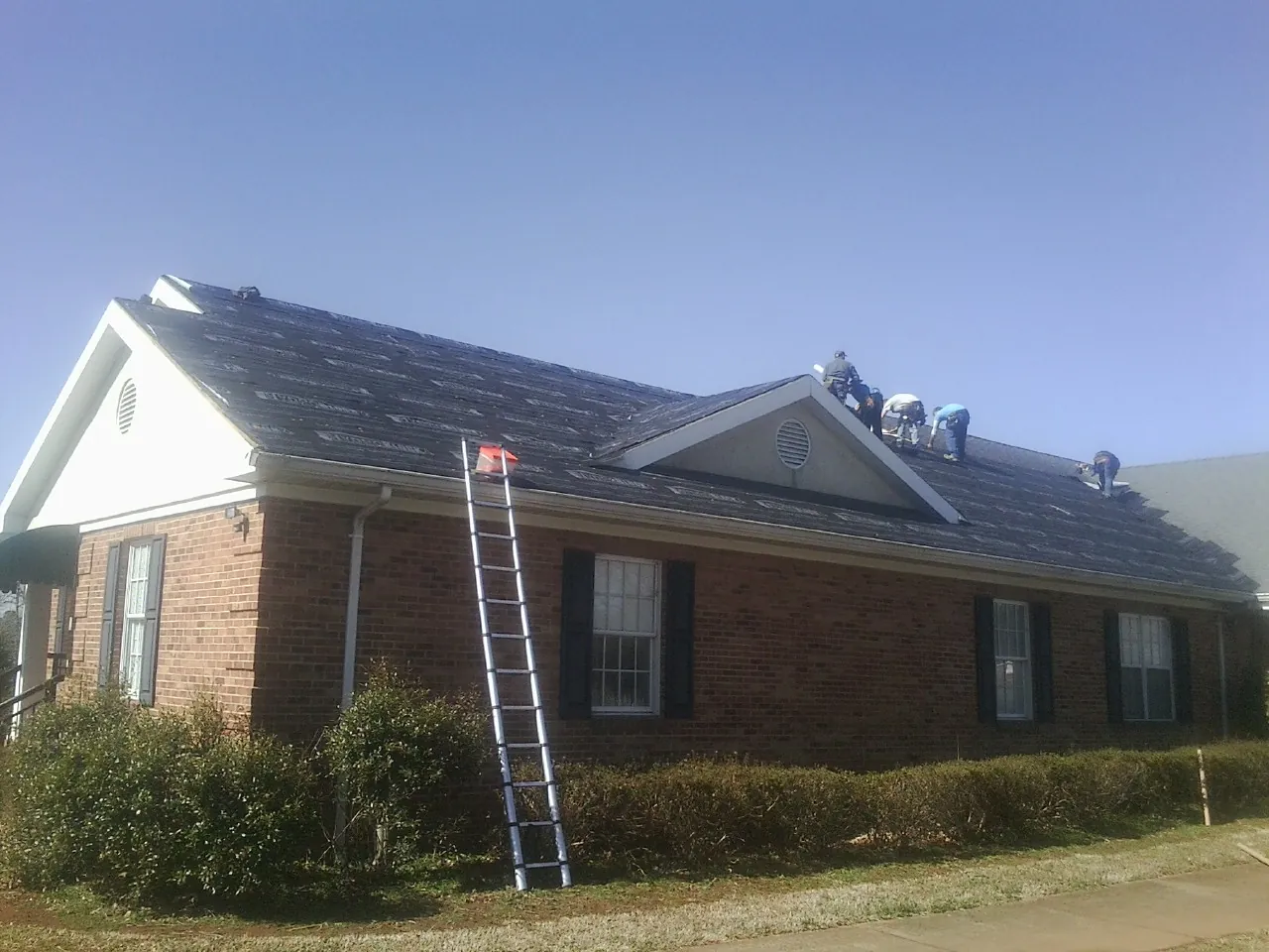 Crew tearing shingles off a brick ranch roof with a ladder set — Emergency Roof Repair work by our crew in Louisburg