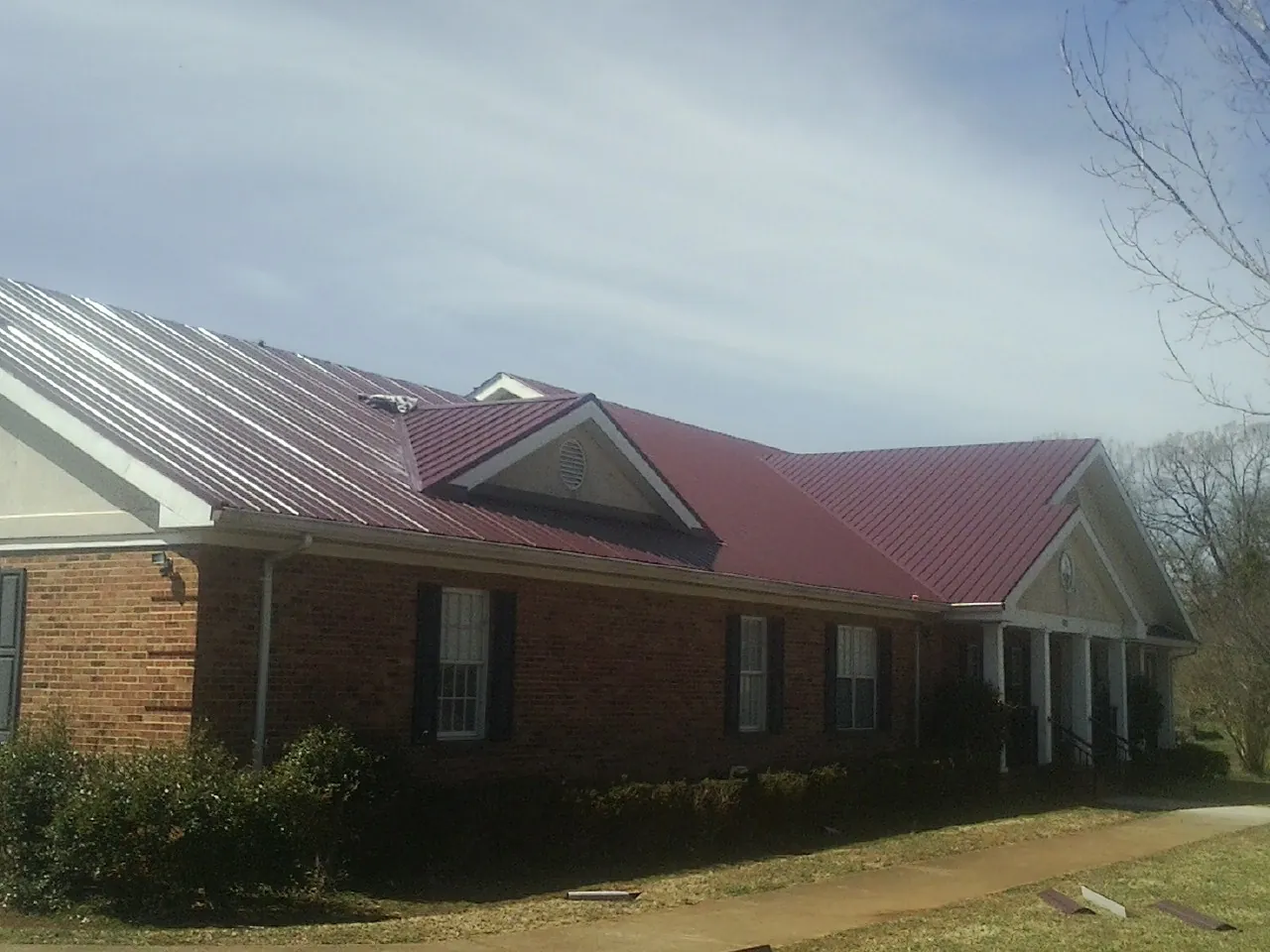 Red metal roof with gabled entries on a long brick building, from a Hail Damage Roof Repair job in Louisburg