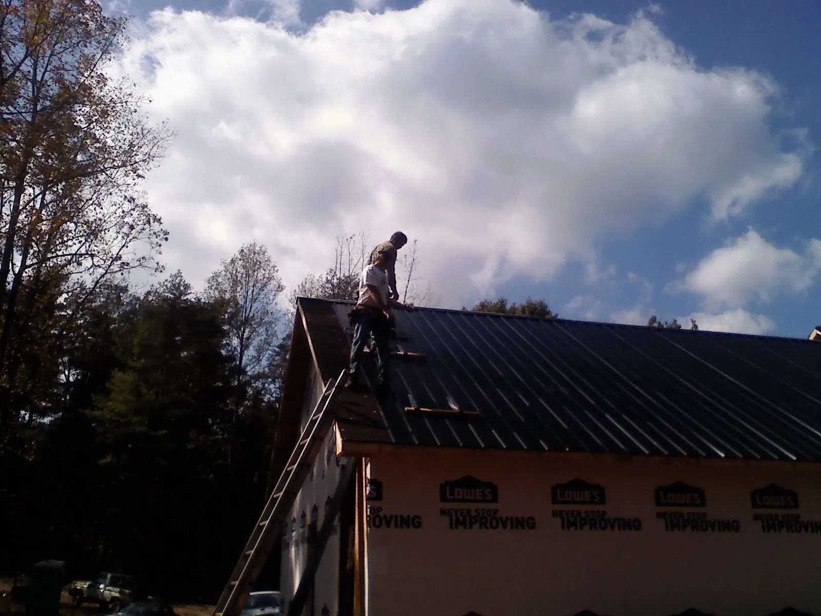Roofer fastening dark metal panels high against a cloudy sky, from a Roof Inspection job in Louisburg