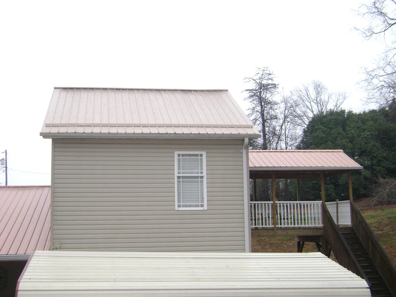 Tan metal roofs on a two story addition and attached porch, from a Roof Replacement job in Louisburg