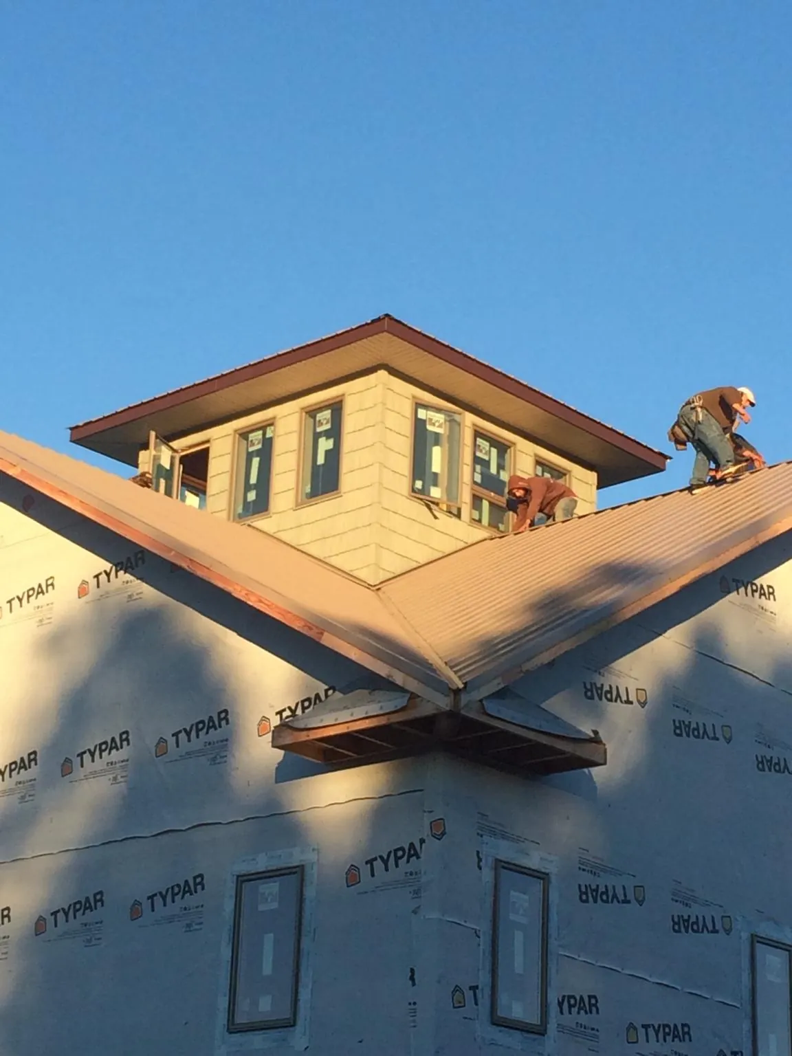 Roofers working around a rooftop cupola on a new metal roof at sunset — Roof Waterproofing in Louisburg by Roofing Brothers